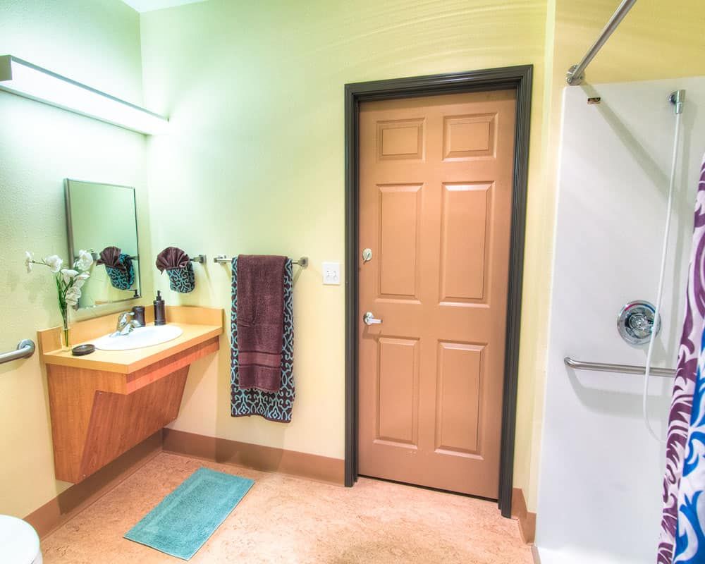 A modern bathroom featuring a large mirror, sink, and a shower with a wooden door.