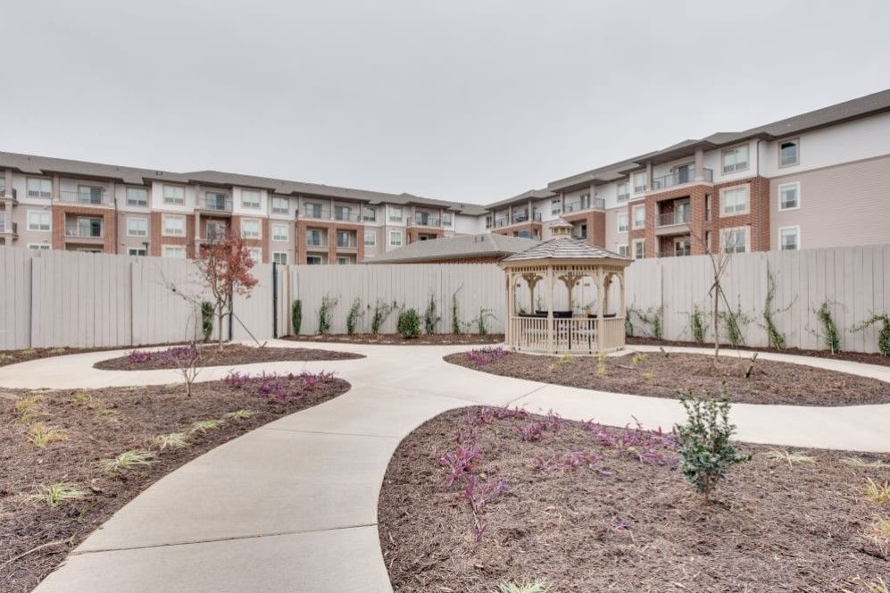 A modern apartment complex with a landscaped outdoor area featuring a pathway and a gazebo.