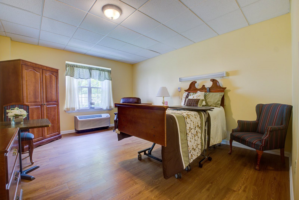 A cozy bedroom with a hospital bed, wooden floor, and natural light from the window.