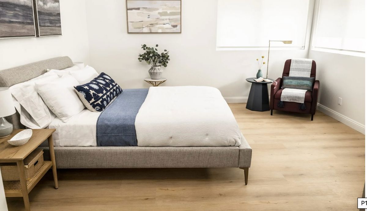 A modern, minimalist bedroom with a neatly made bed, chair, and nightstand.