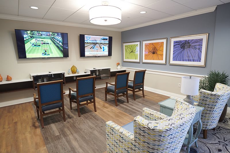 A modern conference room with chairs, tables, wall-mounted TV screens, and colorful artwork.