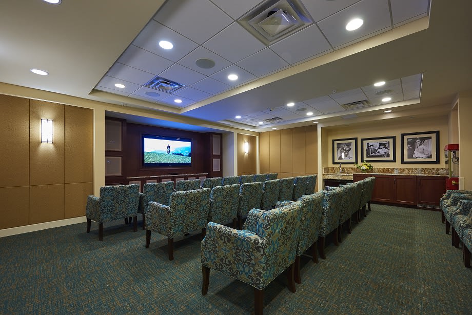 A cozy indoor theater room with rows of comfortable seating facing a large screen.