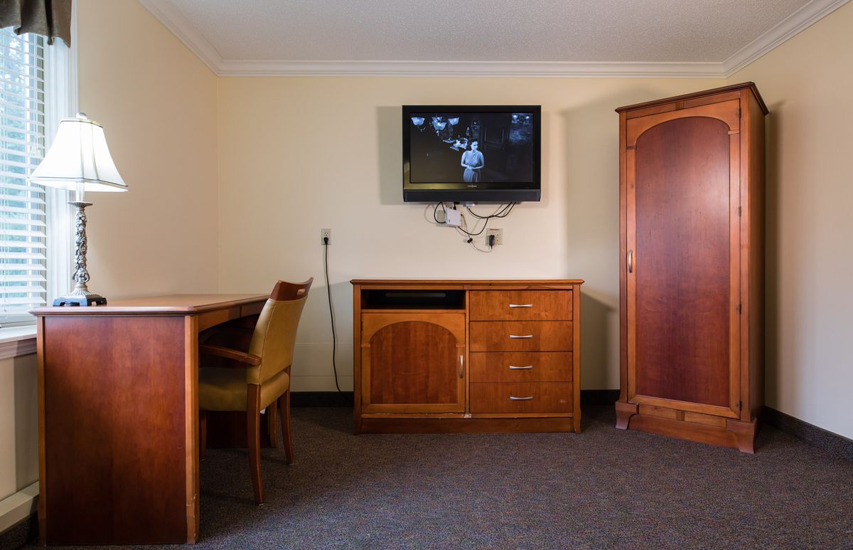 A simple hotel room setup with a wall-mounted television, wooden desk, and cabinet.