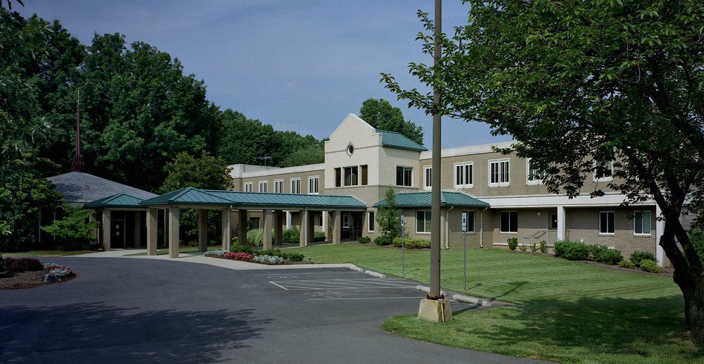 A modern hospital building surrounded by greenery and a driveway leading to the entrance.