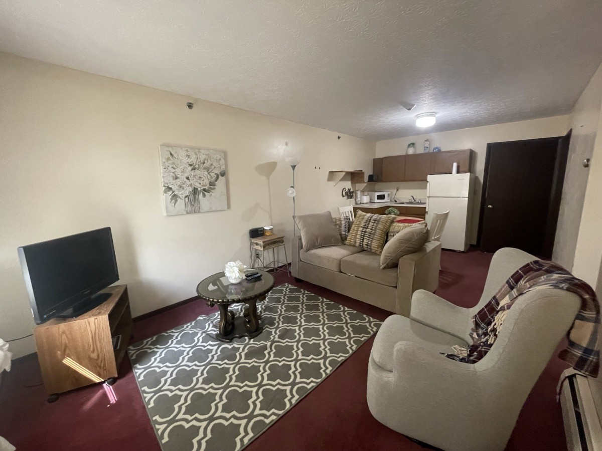 A cozy living room with a sofa, coffee table, and television, adjacent to a small kitchen area.