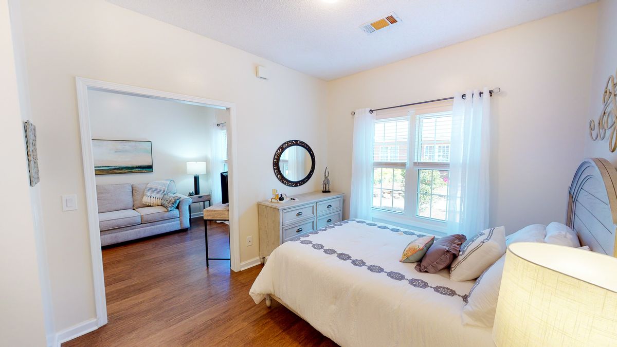 A cozy bedroom with a bed, neutral decor, and a view into the adjoining living area.