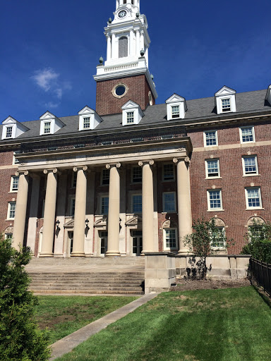 A grand brick building featuring impressive columns and a clock tower, set against a clear blue sky.