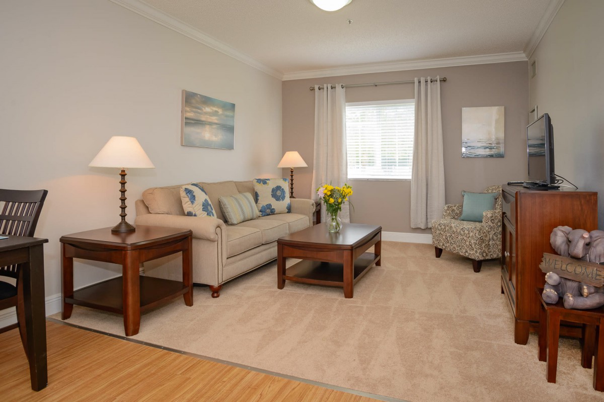 A cozy living room with a sofa, armchair, and coffee table, decorated with lamps and wall art.