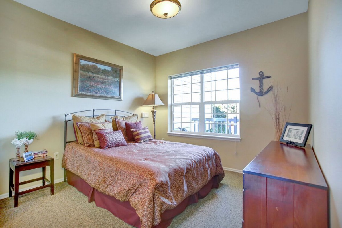 A cozy bedroom with a neatly made bed, warm lighting, and nautical decor on the wall.