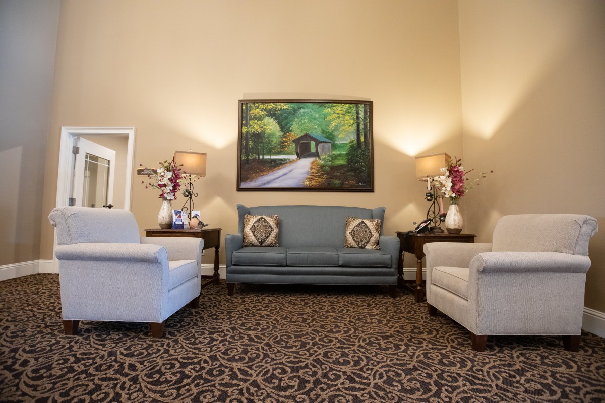 A cozy living room featuring a blue sofa, white armchairs, decorative lamps, and a painting of a scenic landscape.
