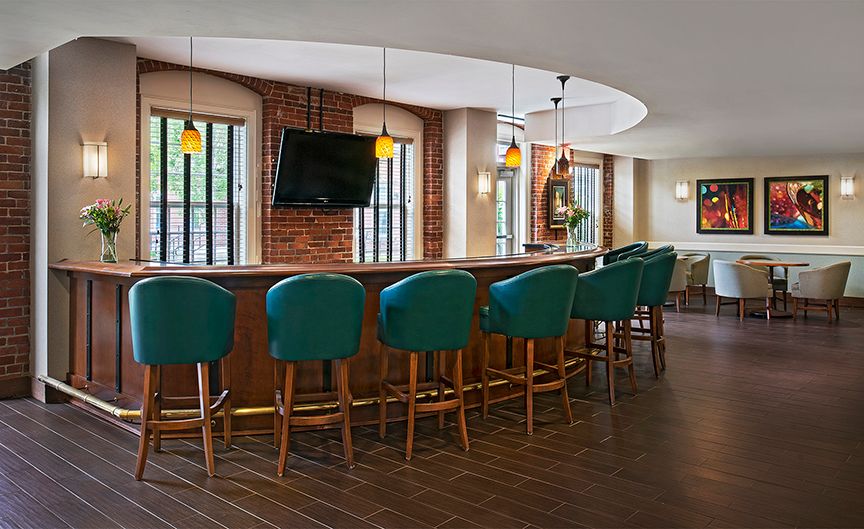 A modern bar interior with teal chairs, a wooden counter, and a wall-mounted TV.