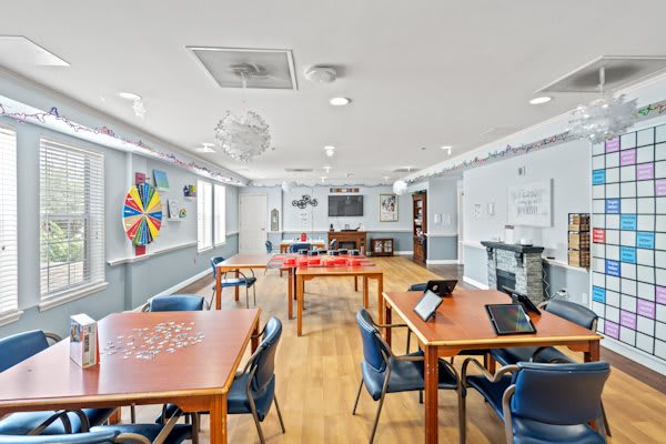 A bright and inviting activity room with tables, chairs, puzzles, and games set up for community use.