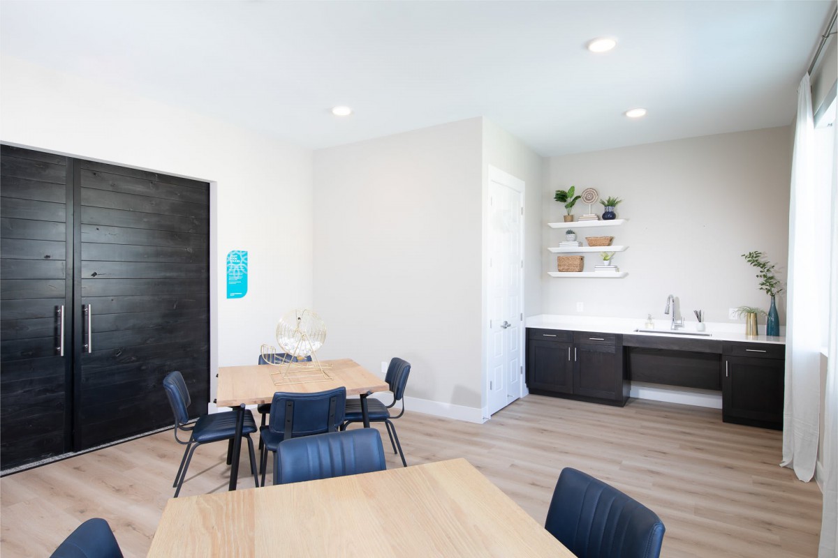 A modern office meeting room with minimalist decor, featuring wooden tables and black chairs.