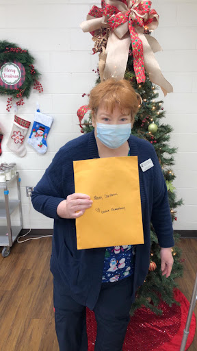 A person holding an envelope in front of a decorated Christmas tree.