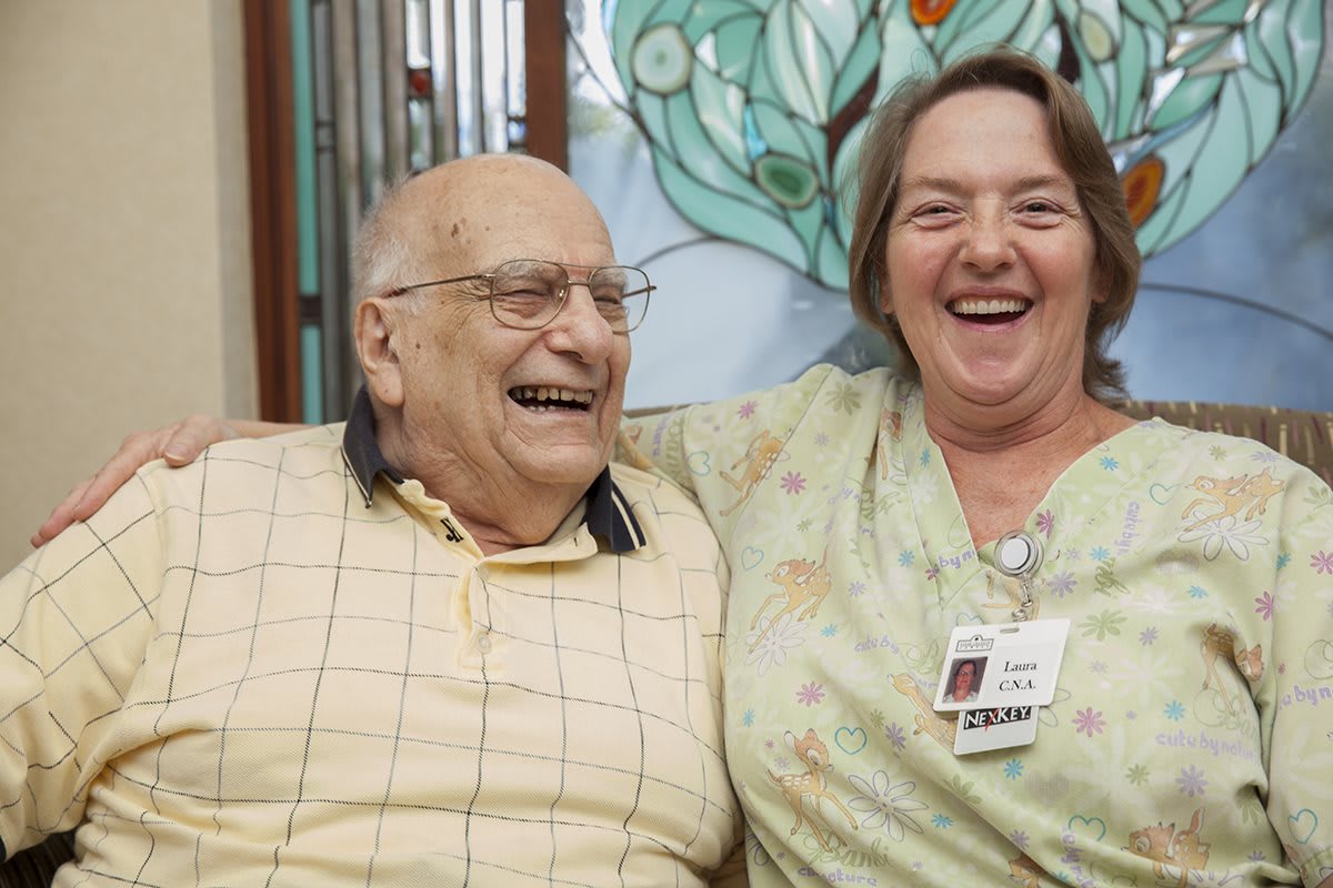 An elderly man and a woman are smiling and enjoying each other's company indoors.