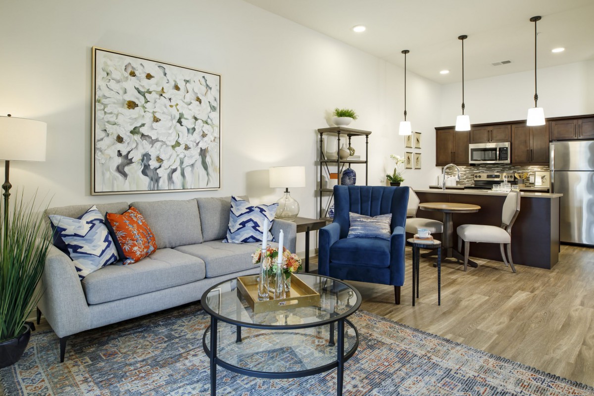 A contemporary living room with modern decor, featuring a cozy sofa, armchair, and stylish coffee table. The open layout extends to a dining area with pendant lighting.