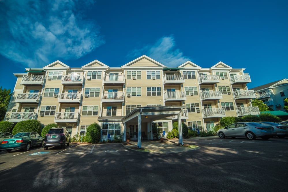 A four-story apartment building with a parking lot in front on a sunny day.