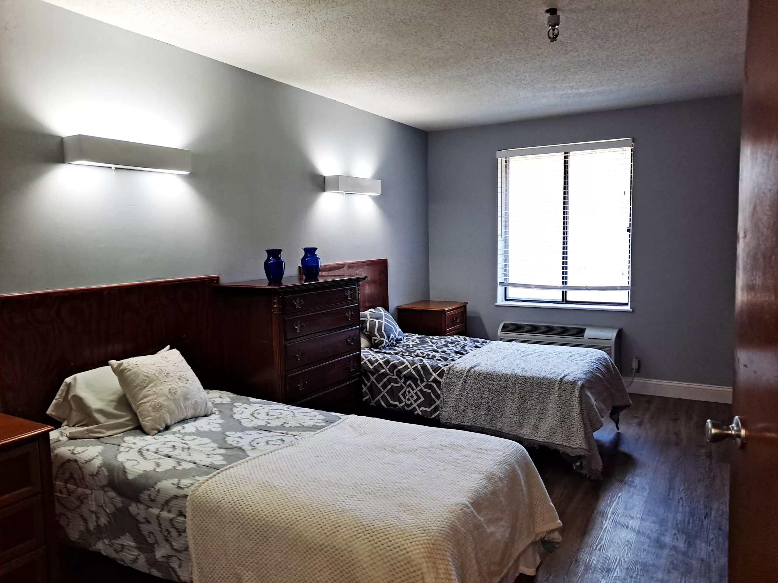 A cozy bedroom featuring two single beds, wooden furniture, and a window allowing natural light.