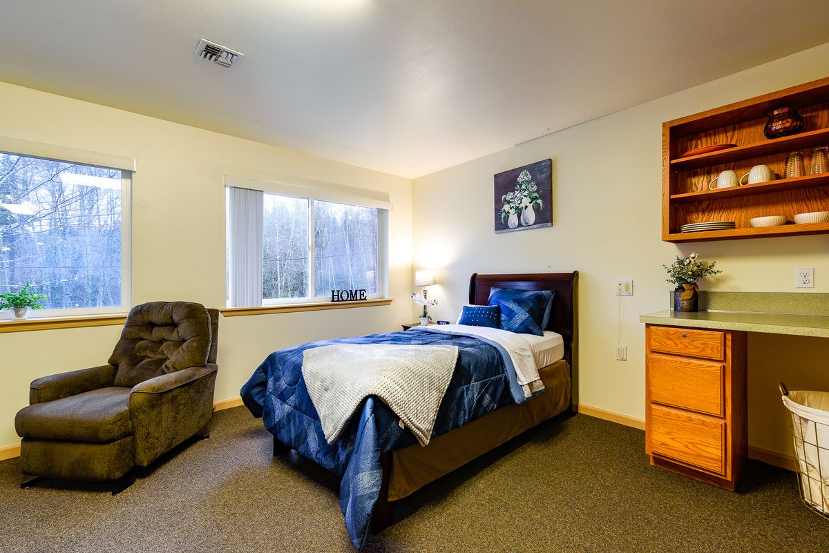 A cozy bedroom with a comfortable bed, armchair, and a window letting in natural light.