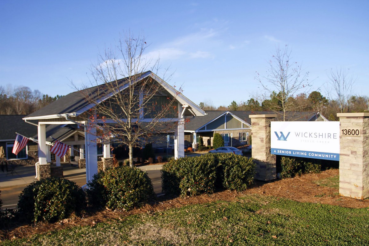 A building with a prominent sign in front, surrounded by shrubbery under a clear blue sky.