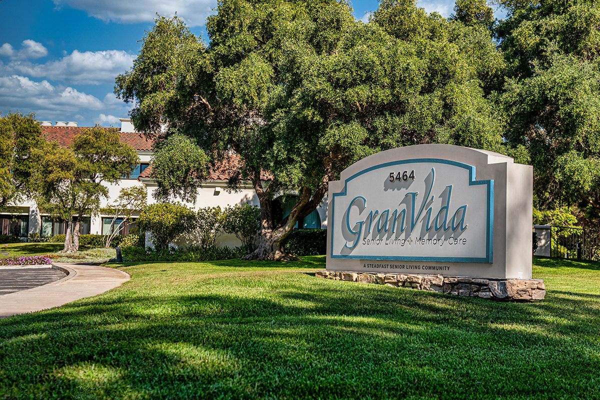 A view of a building with a GranVida sign surrounded by trees and grass.