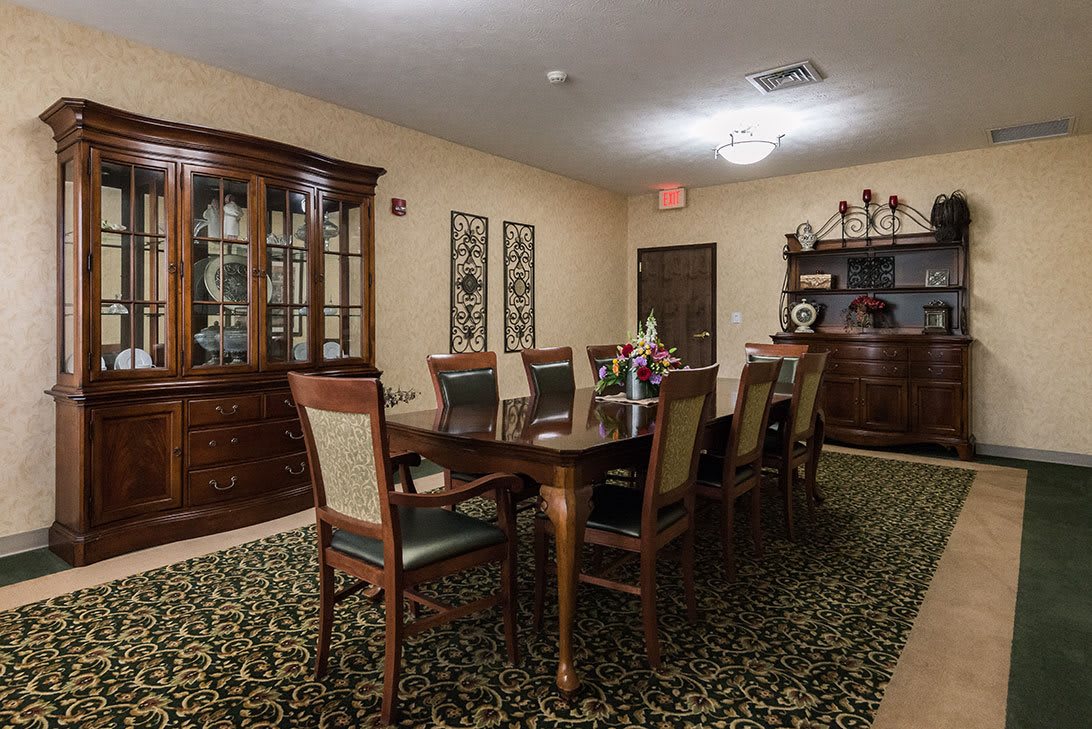 A well-furnished dining room with a large table and chairs, carpeted floor, and a china cabinet.