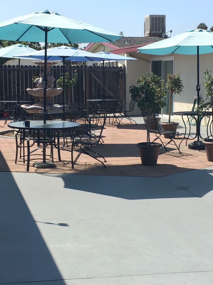 An outdoor patio area with tables, chairs, and umbrellas, featuring a central fountain and potted plants.