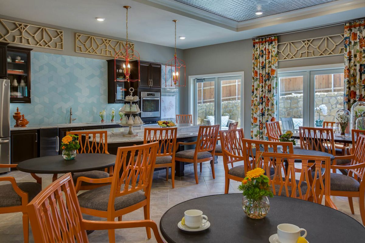 A modern dining room with wooden chairs and tables, featuring a bright and welcoming kitchen area.