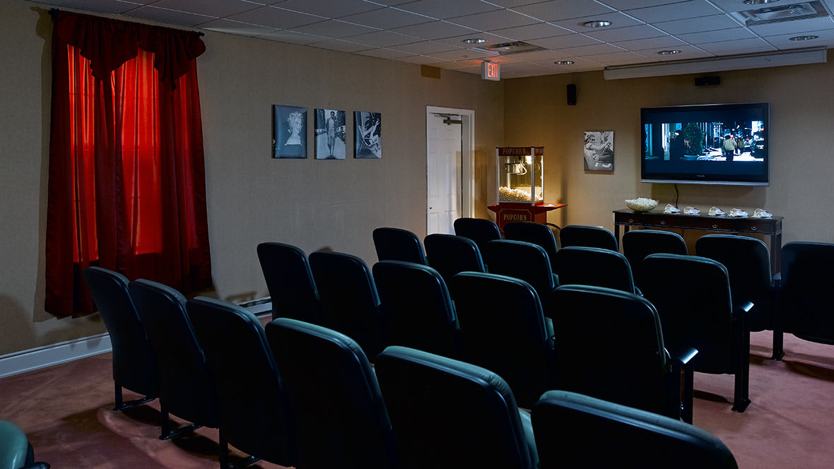 An empty small theater room with rows of seats facing a screen.