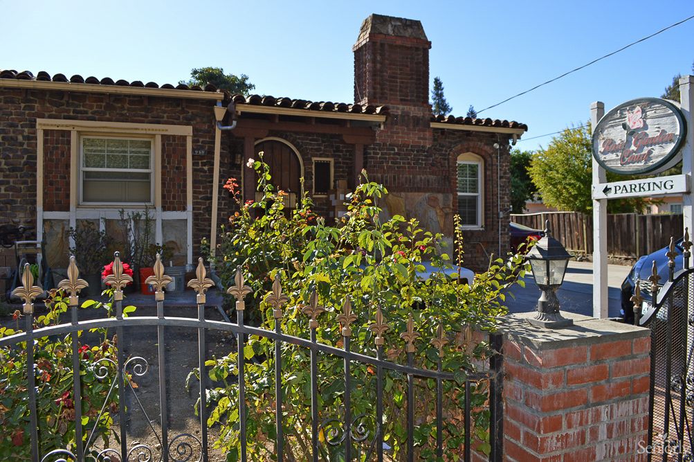 A charming brick house with a chimney, surrounded by a garden and iron fence.
