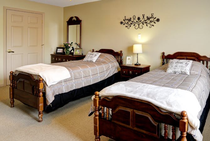 A cozy bedroom featuring twin beds with wooden frames, a lamp on a bedside table, and elegant wall decor.
