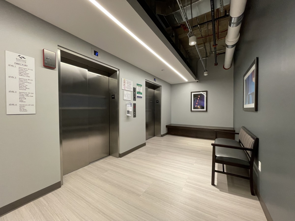 A modern corridor with elevators and a bench, featuring sleek interior design.