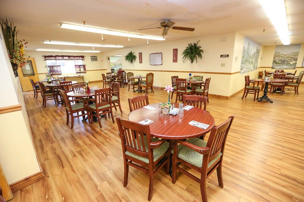 A spacious dining area with wooden tables and chairs, decorated with plants.