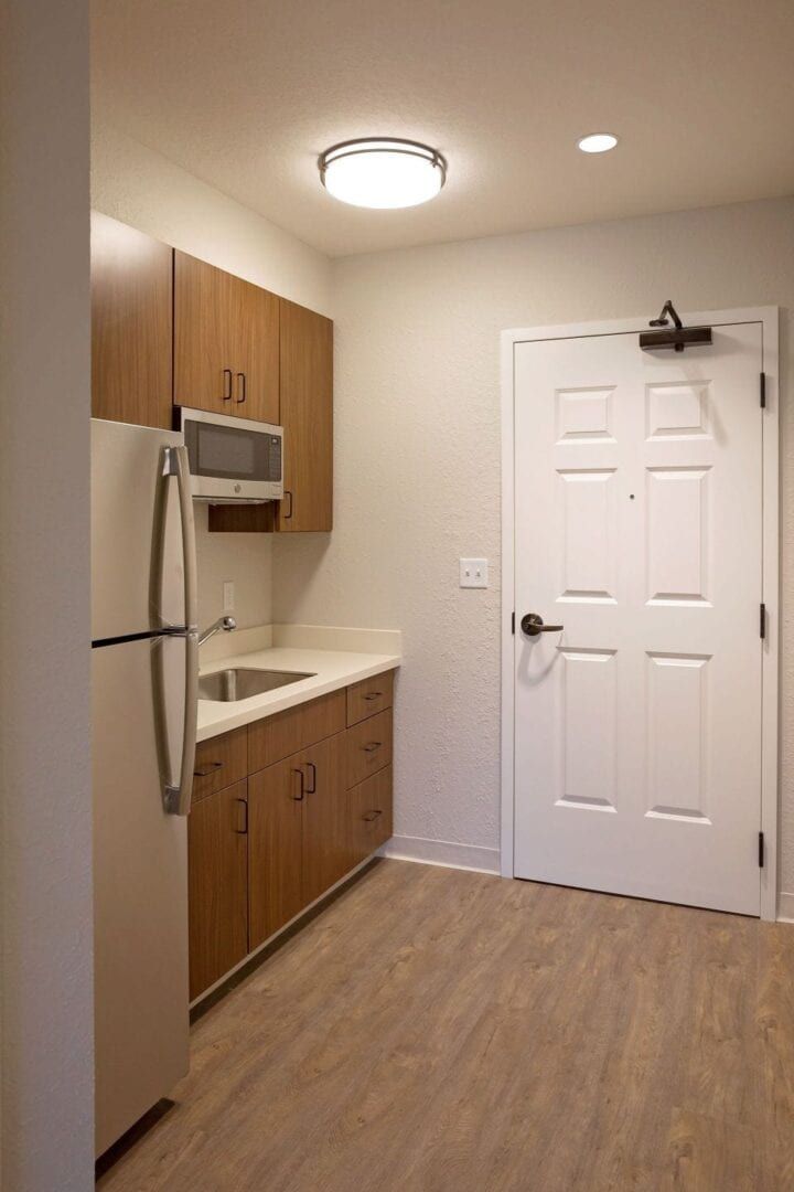 Compact kitchen in a modern apartment with wooden cabinetry, microwave, and refrigerator.