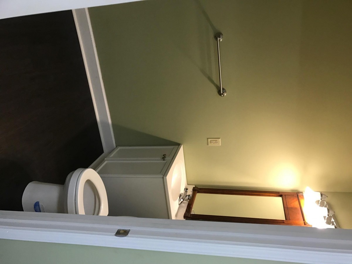 A small bathroom with a toilet, sink, mirror, and towel rack under warm lighting.
