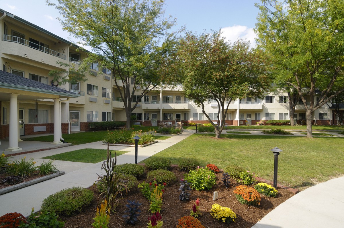 A well-maintained apartment complex with a landscaped courtyard featuring trees and flower beds.