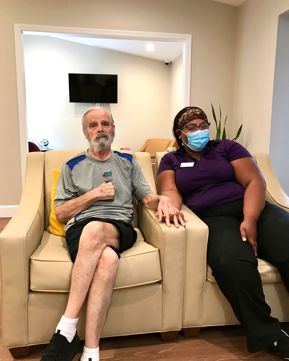 An elderly man and a caregiver sitting together on a sofa indoors.