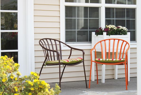 Two colorful chairs on a patio next to a window with plants.