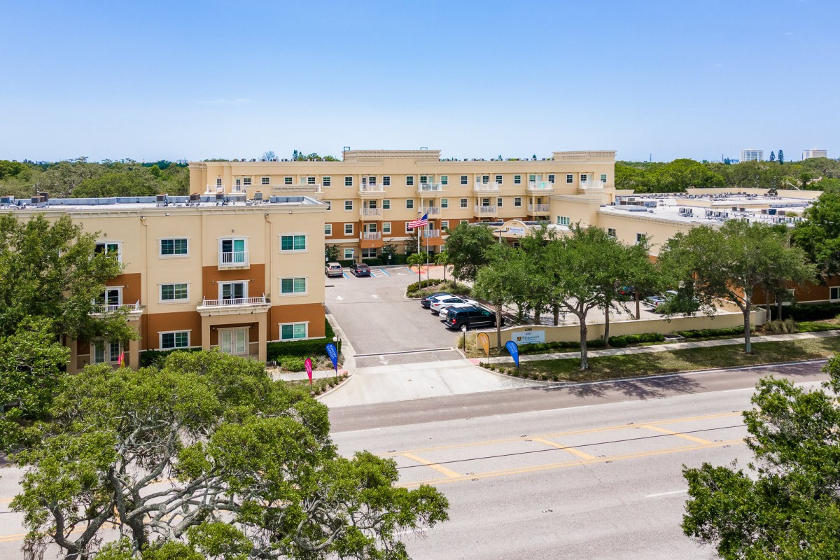 Aerial view of a residential apartment building with a parking lot and trees lining the street.