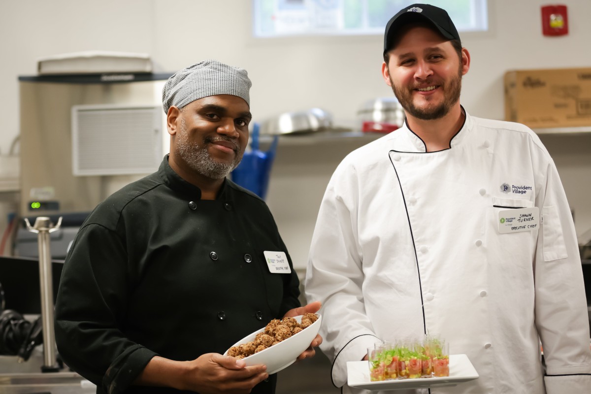 Two chefs proudly display their culinary creations in a professional kitchen.