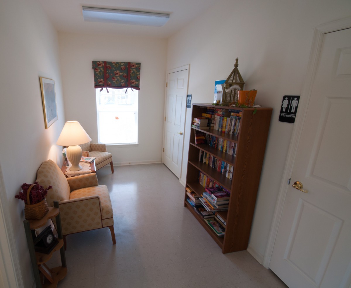 A small waiting room with chairs, a bookshelf, and a window.