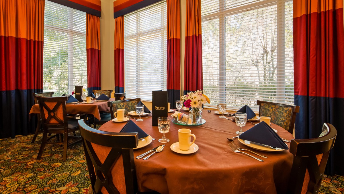 An elegantly set dining table in a restaurant with large windows and colorful curtains.