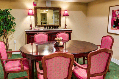 A cozy dining area featuring a round wooden table surrounded by pink upholstered chairs, complemented by a mirror and lamps on the sideboard.
