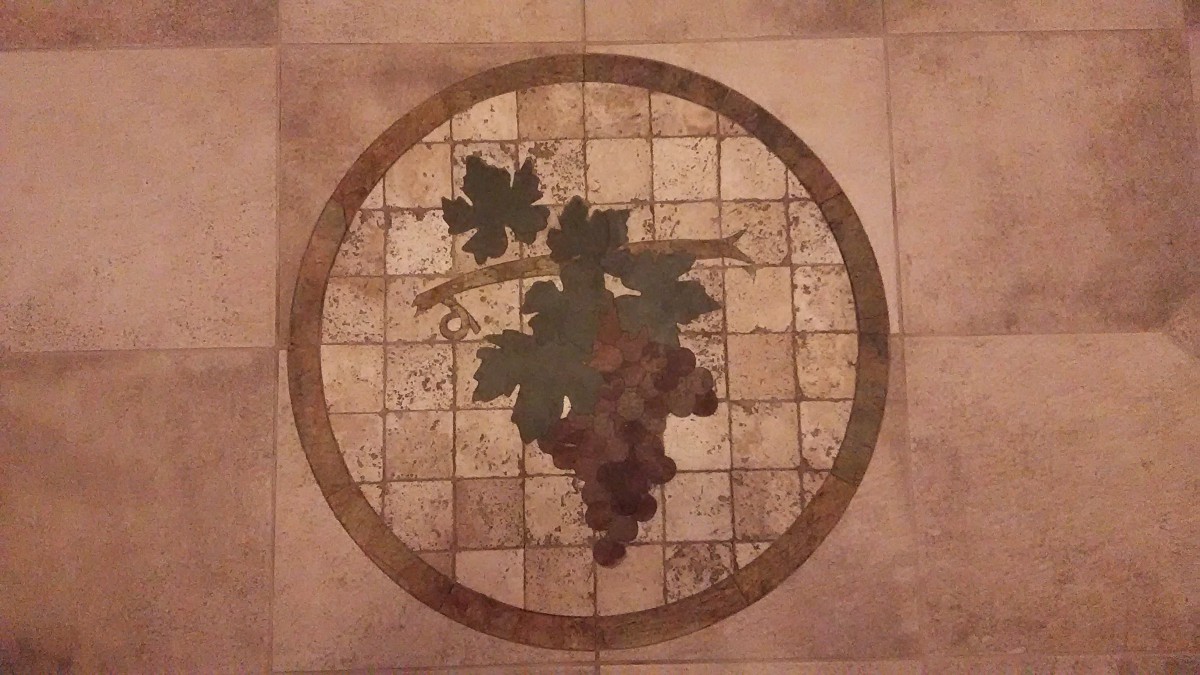 A decorative tile featuring a mosaic of grapes and vine leaves within a circular border.
