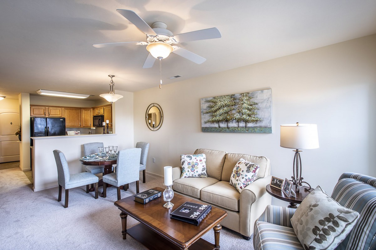 A cozy living room with a sofa, coffee table, dining area, and ceiling fan.