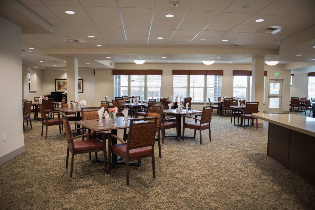 A spacious dining area with neatly arranged tables and chairs, illuminated by natural light from large windows.