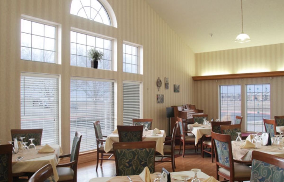 A well-lit dining room with large windows, tables, and chairs arranged neatly.