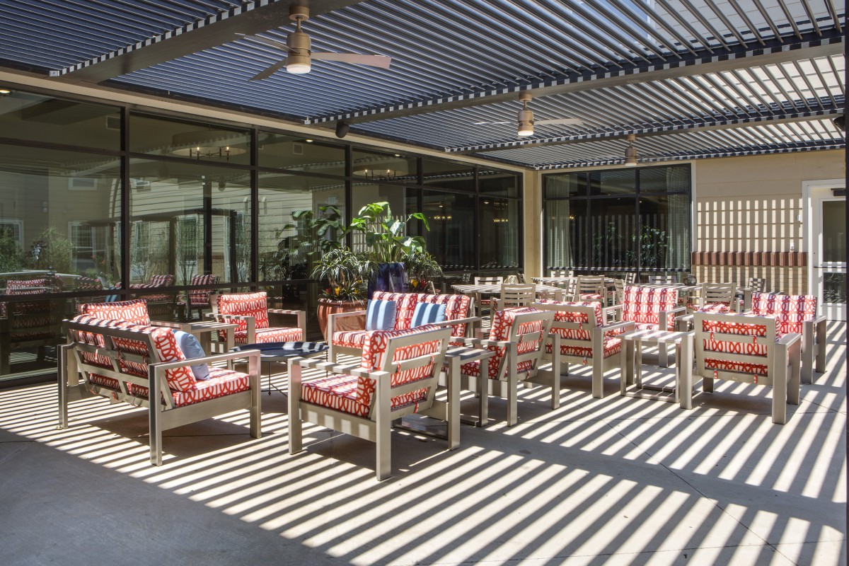 A stylish outdoor patio with colorful seating under a pergola casting striped shadows.