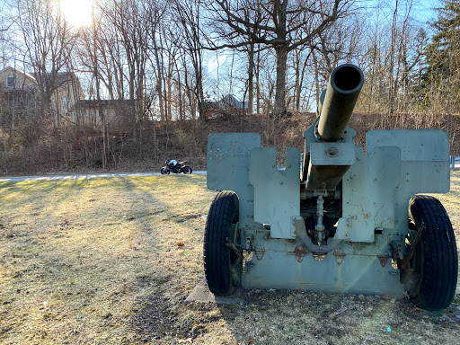 A vintage cannon facing forward in an outdoor setting, surrounded by trees.
