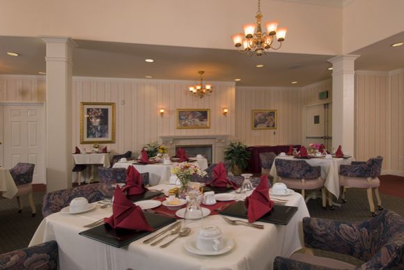 An elegant dining room setup with tables adorned with red napkins and decorative place settings.
